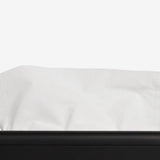 A close-up of a white tissue paper partially pulled from a matte black tissue box dispenser against a clean white background.