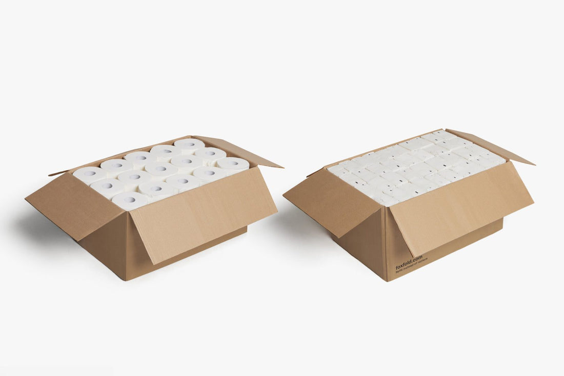 Two open brown cardboard boxes containing multiple white toilet paper rolls, compared to  fox fold toilet paper.